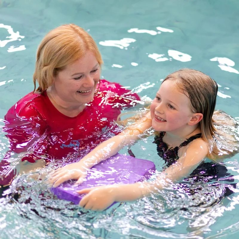 A Big Squids instructor supporting a child swimming with a float